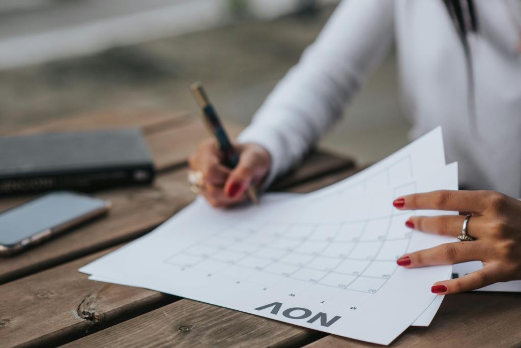 A woman planning with a calendar outdoors, jotting down notes on a wooden table with a pen.